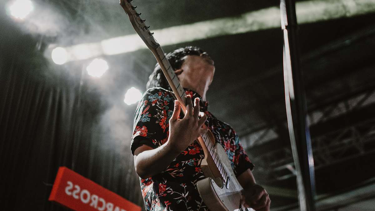 leisure activities man wearing black and red floral collared button-up shirt standing while playing electric guitar musical instrument